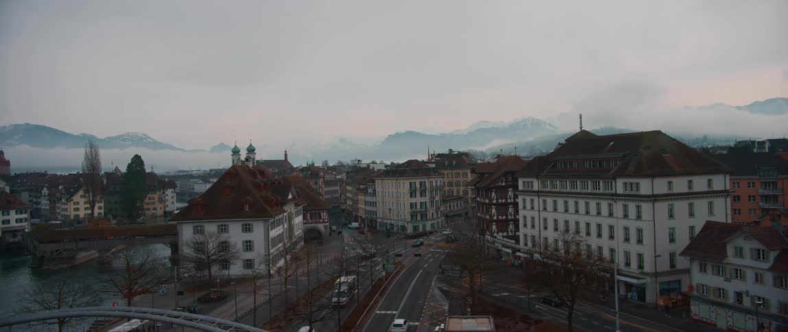 Traffic moves through town cut through by river as fog covers the mountains on the horizon