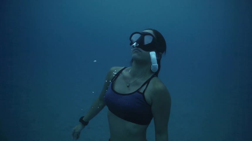 A female snorkeler slowly rises to the surface from the sea floor