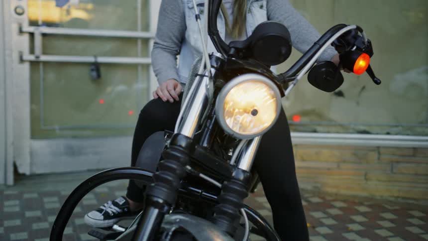A woman is sitting on a parked motorcycle in a city