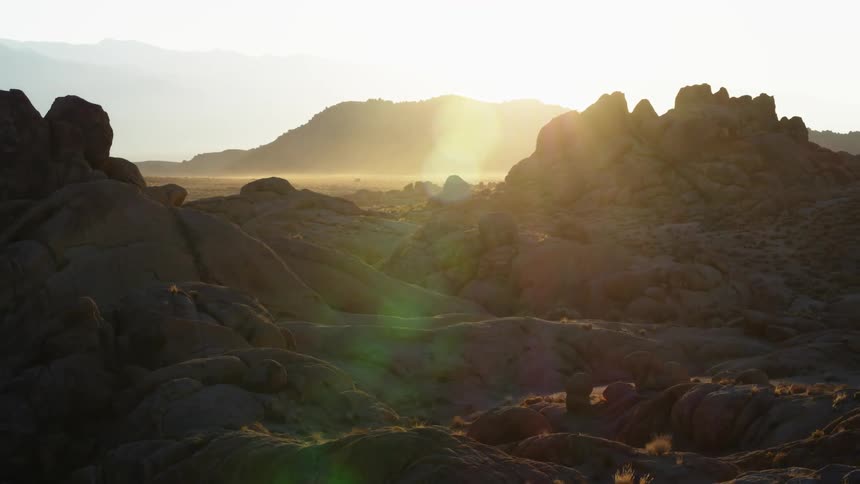 Large rocks sit next to a field as mountains sit in the distance on a sunny day