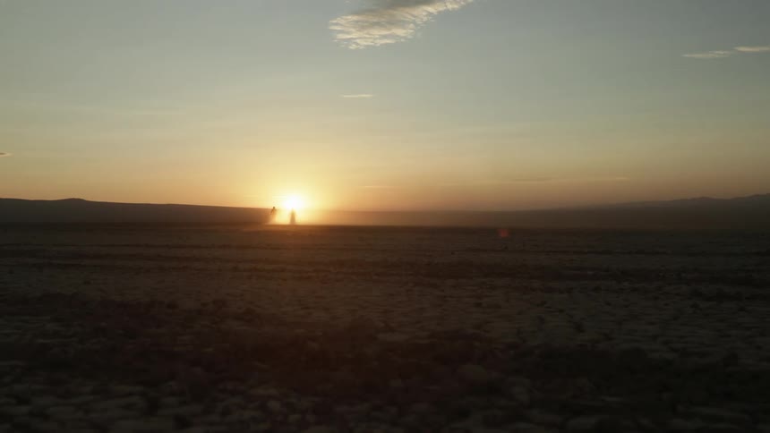 Two motorcycles travel in the desert towards the setting sun