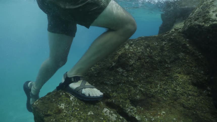 Man swims underwater towards the rocks then climbs up the rocks to exit the water