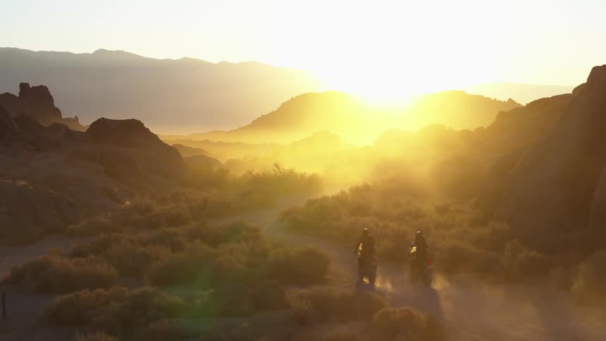 Two motorcyclists ride down a winding dirt road in a canyon