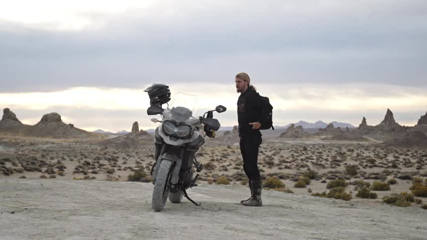 A man is standing by his parked motorcycle in a deserted area
