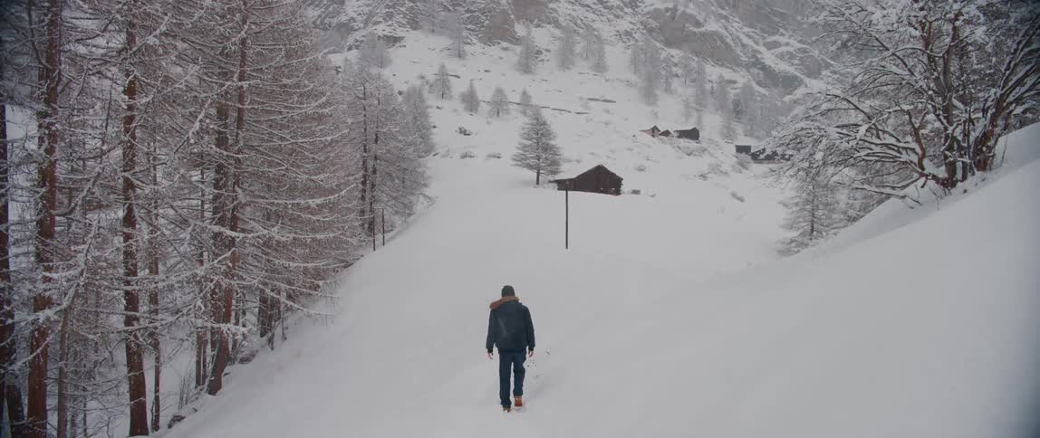 A man walks through a snowy field near a forest