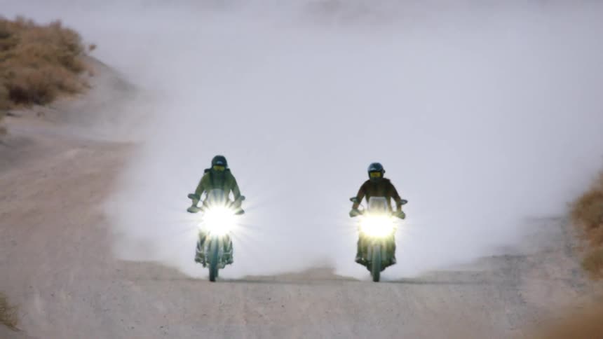 Two people are riding motorcycles through the wilderness
