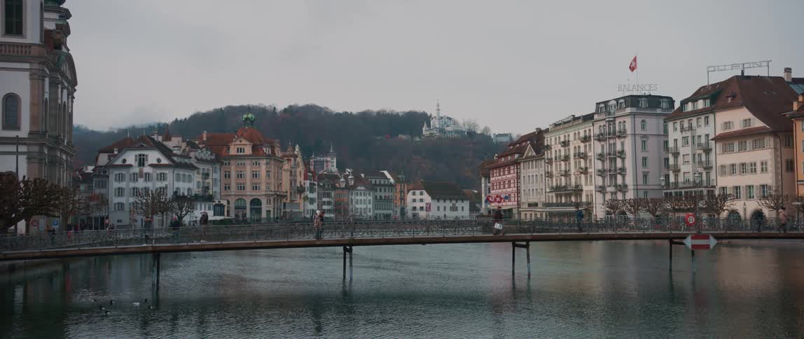 People cross the bridge over river between buildings