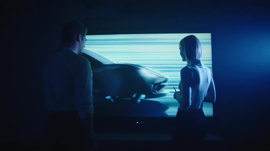 A man and woman walk towards a television with a car racing on it