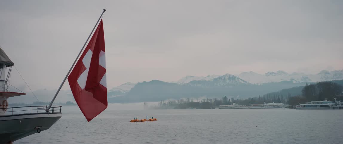 Boats on the water with a mountain range in the distance and the Swiss flag in front