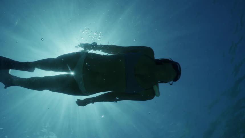 Woman wearing a bikini swimming underwater under the sun in the blue ocean waters