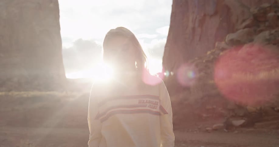 Blonde woman brushing back her hair while standing between two large rocks at sunset
