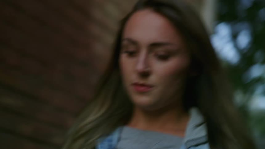 A woman tucks her long hair behind her shoulder while walking down an alley