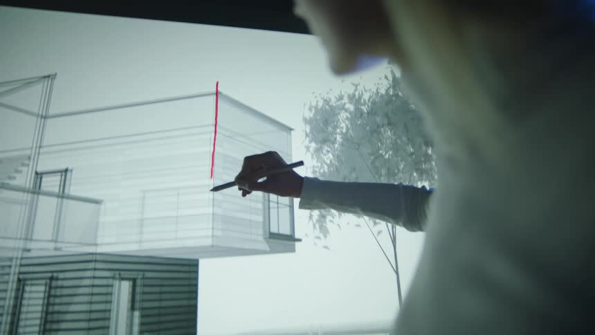 An architect in an office draws a line on a building on a screen