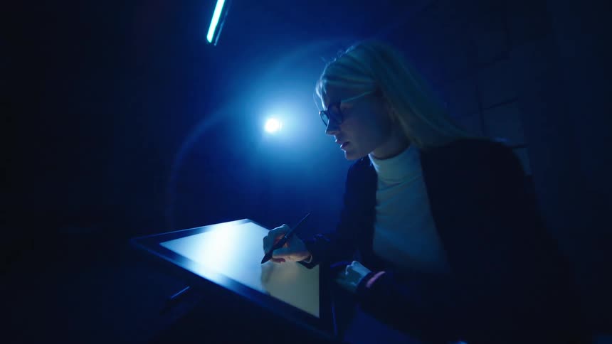 A woman is working on a tablet in a dark room