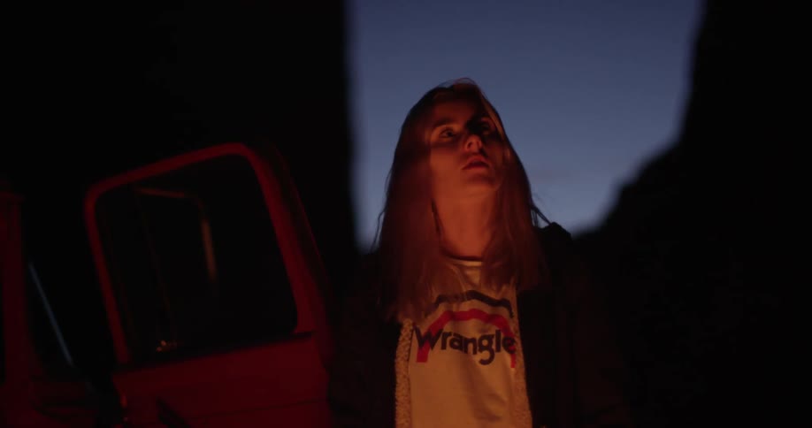 A woman is standing near a campfire looking up at the sky