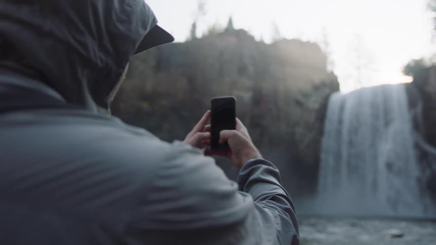 A man uses his smartphone to photograph a waterfall