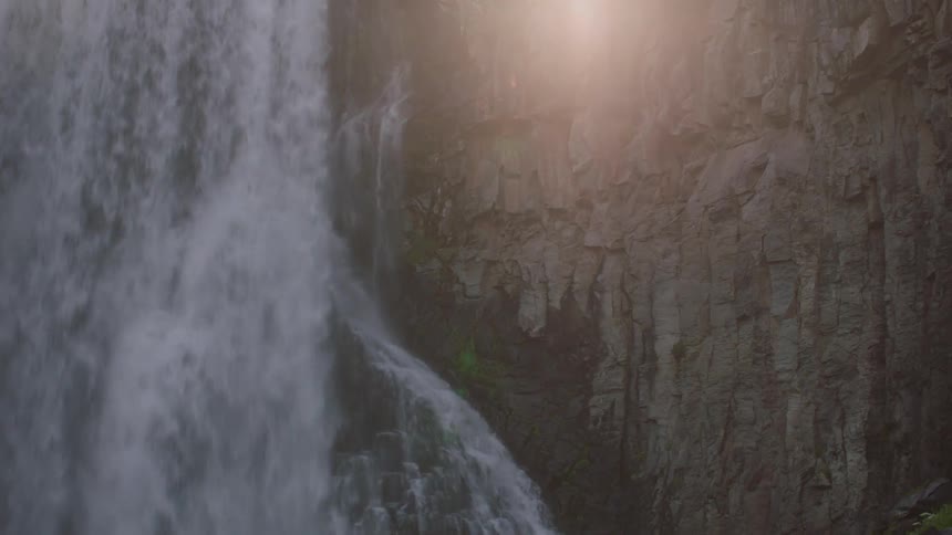 Light brightens cliff wall as waterfall flows down like a sheet and pours down slope