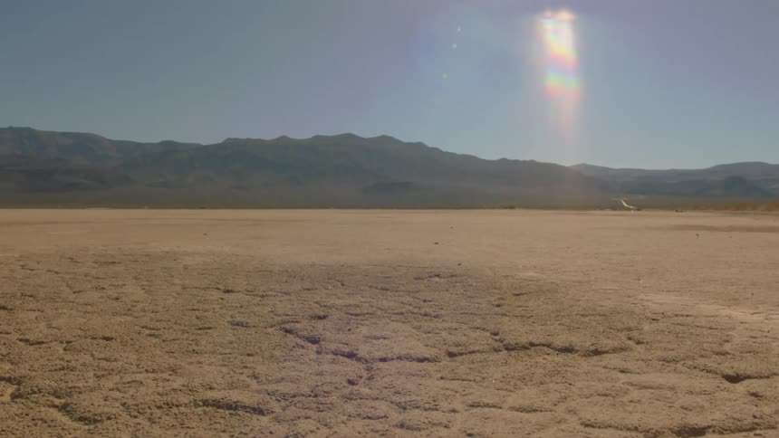 View of barren desert with distant mountains under sun