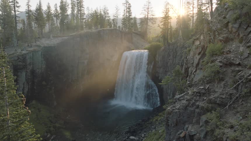 An aerial view of a waterfall crashing down in to a river in a forest