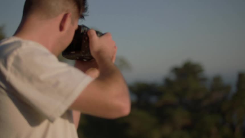 A man takes photos with a dslr camera while standing near the woods