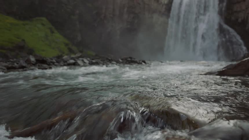 A waterfall plunges into a river that moves over smooth rocks