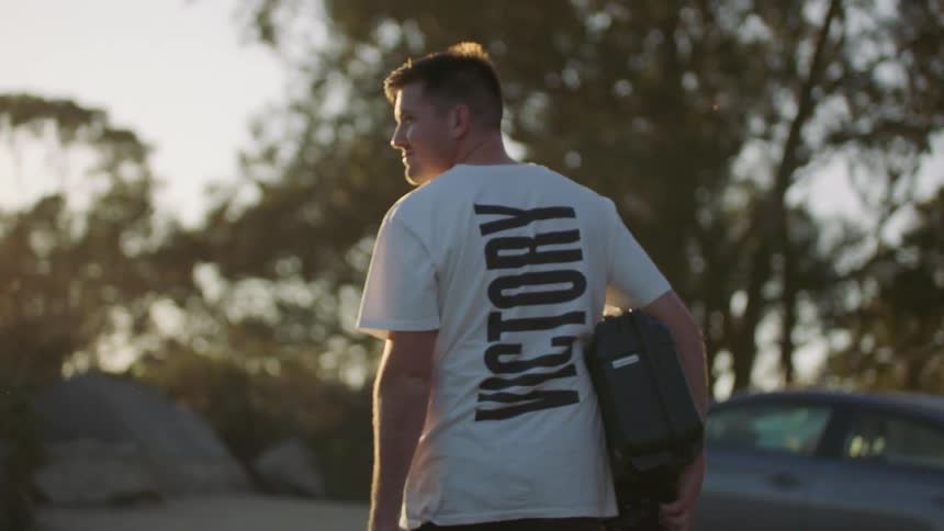 A man carrying a camera and equipment cases looks back and smiles on his way to the car