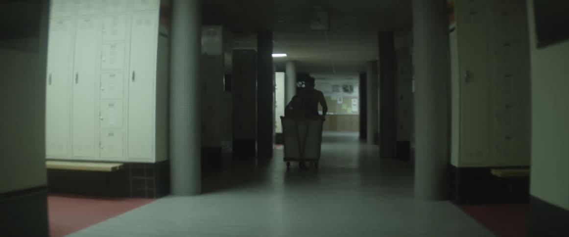 A man pushes a woman in a crate through a locker room