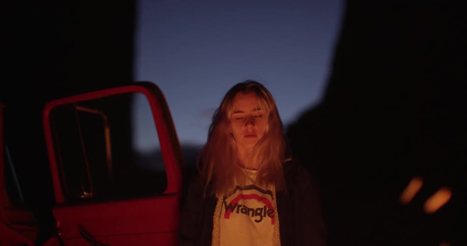Sparks flying up from a campfire as a blonde woman looks upon them