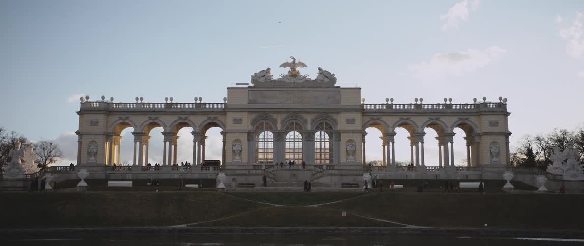 Tourists mingle near an ornate monument with trees on each side under a blue sky