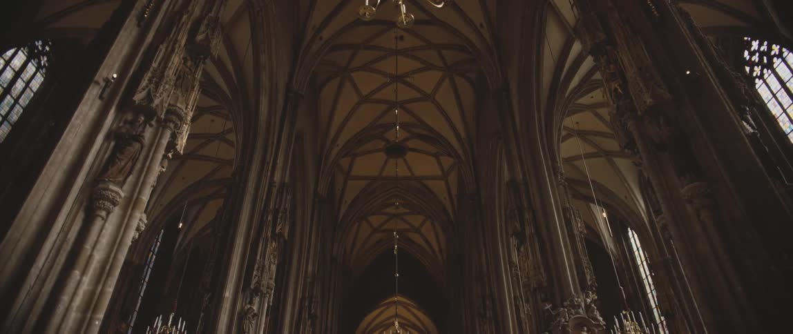 Sunlight comes through windows and shines onto cathedral ceilings and chandeliers in dark wood accented chamber