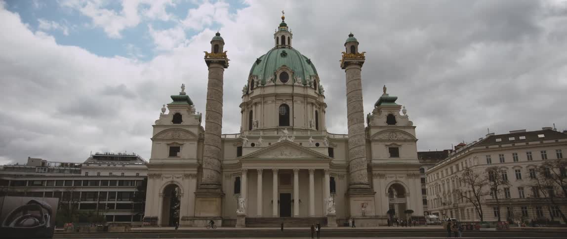 Pedestrians move around cathedral and nearby buildings on cloudy day