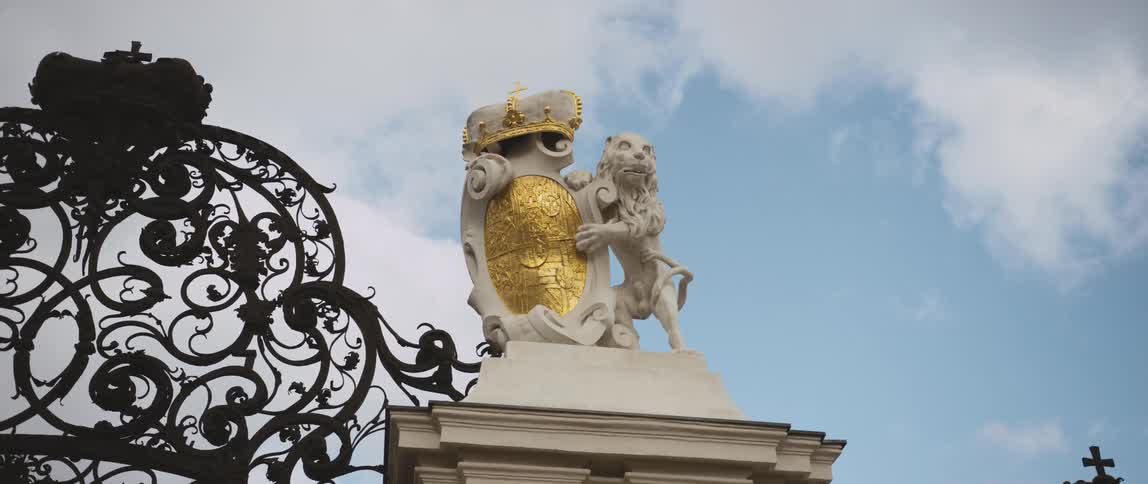 A sculpture of a lion and a shield atop an elaborate fence during the day