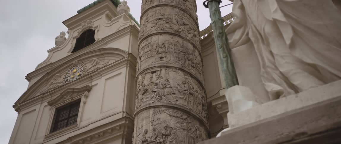 Exterior of a large building with intricate ornate designs and a statue on the right and a clock with roman numerals on the left