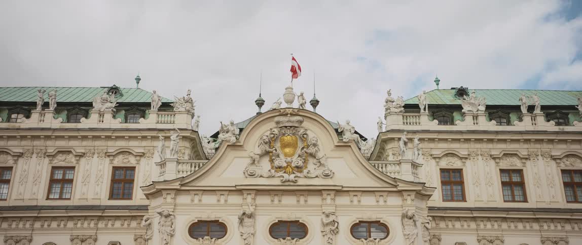 Statues and a flying red and white flag on the rooftop of a landmark under a cloudy blue sky