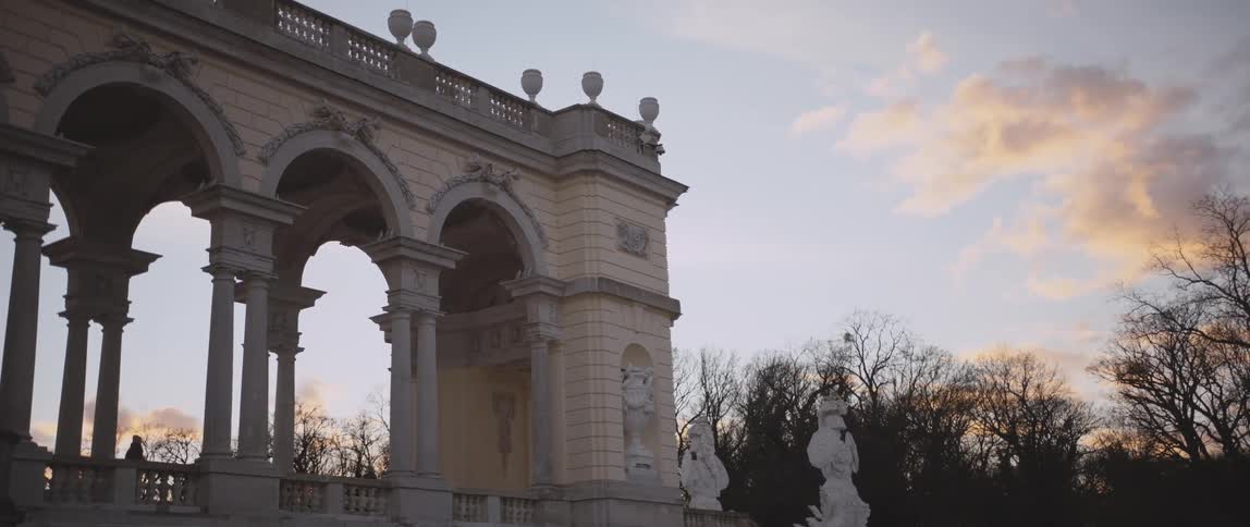 People move around ornate structure under sun highlighted clouds near leafless trees