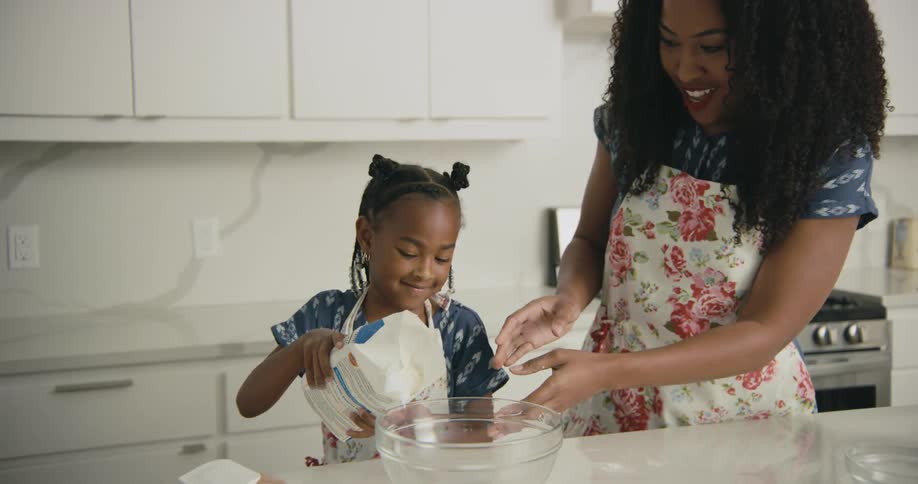A woman helps her daughter pour a bag of flour into a mixing bowl