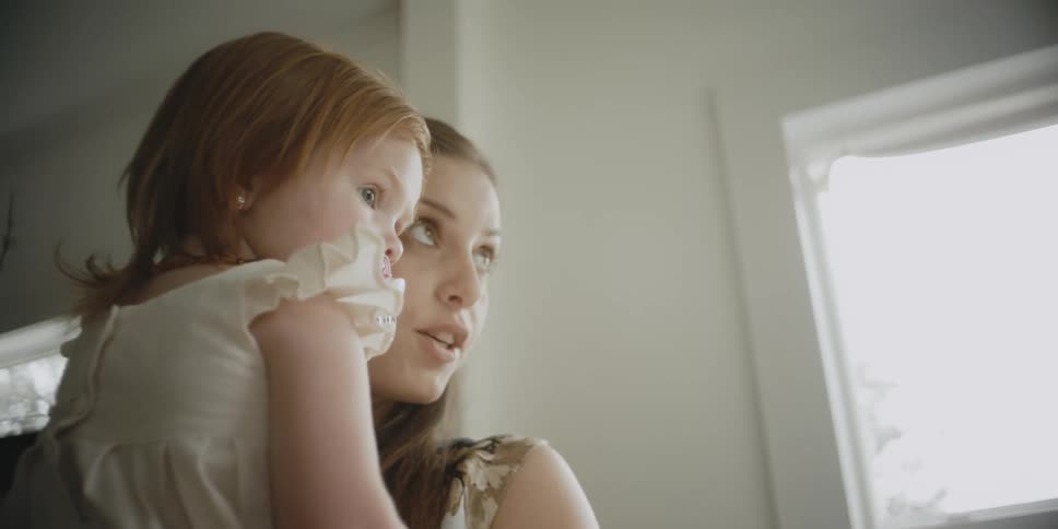Woman holding a child in a living room on a sunny day