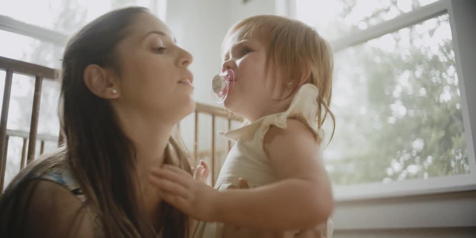 A woman is comforting and interacting with a toddler in a bedroom