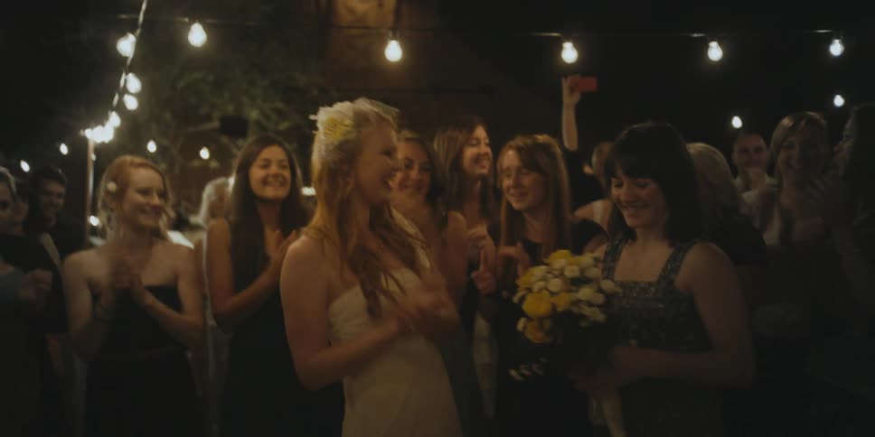 A bride hugs a guest at an outdoor wedding reception as everyone applauds