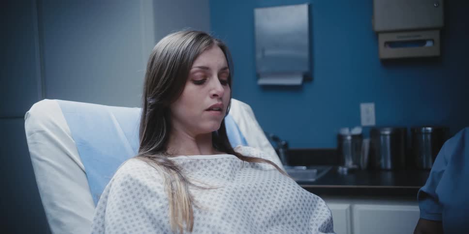 A woman in a hospital gown sits on a bed