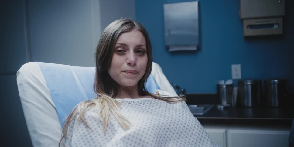 A worried looking woman lays on an examination table wearing a hospital gown