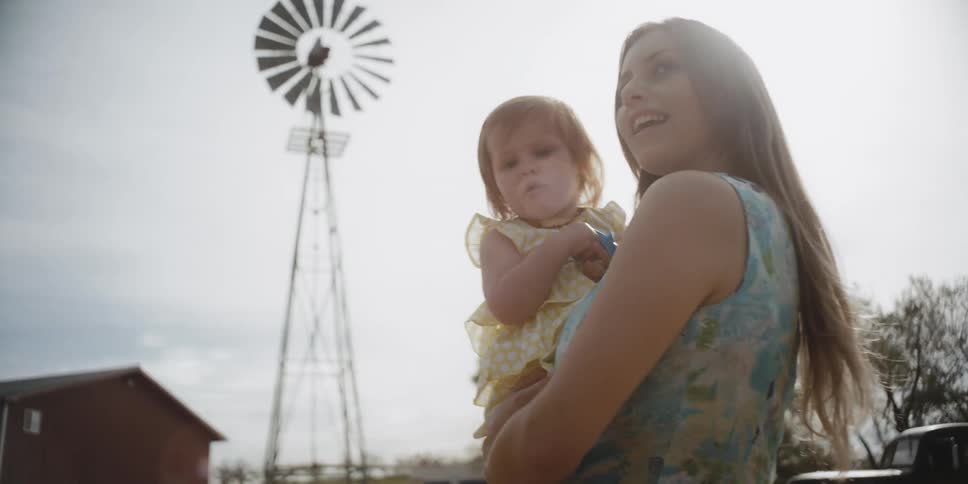 A woman is carrying a baby past a windmill