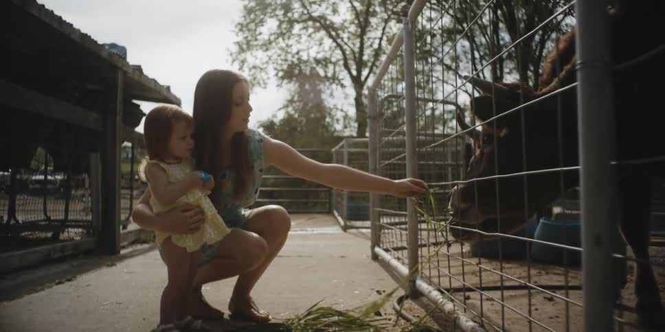 Woman holding a small child and feeding an animal in a pen