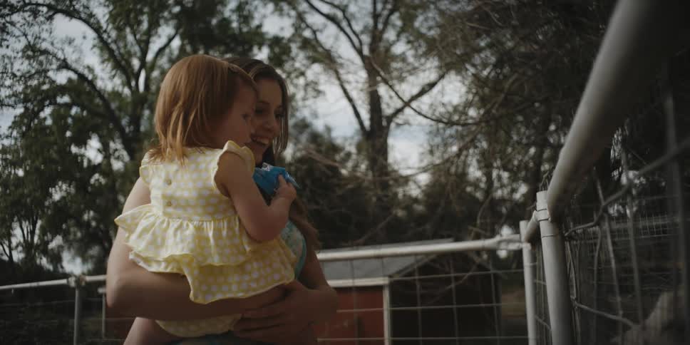 A woman is carrying a baby towards a fence