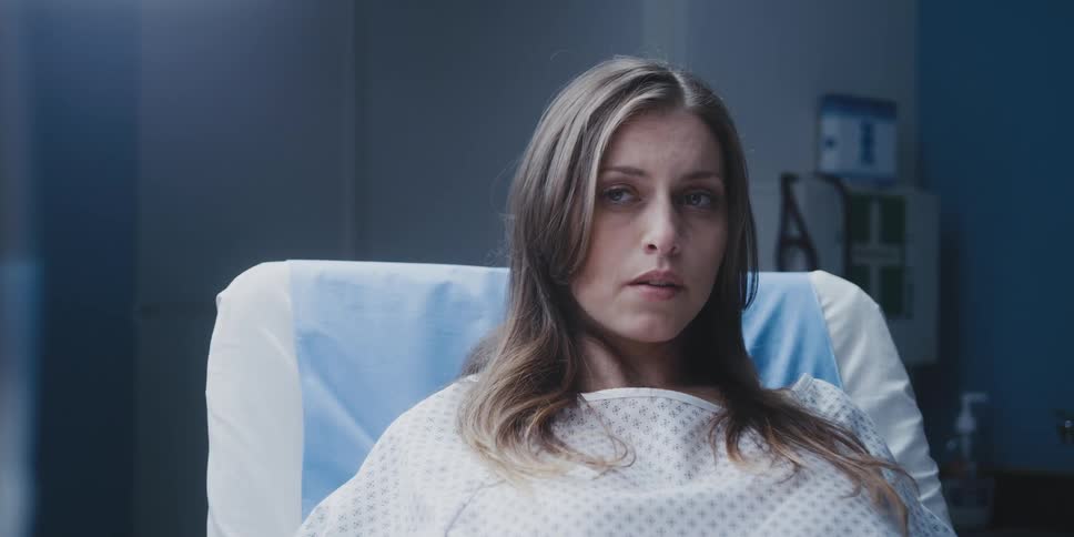 A woman is breathing deeply and thinking as she sits in a hospital gurney