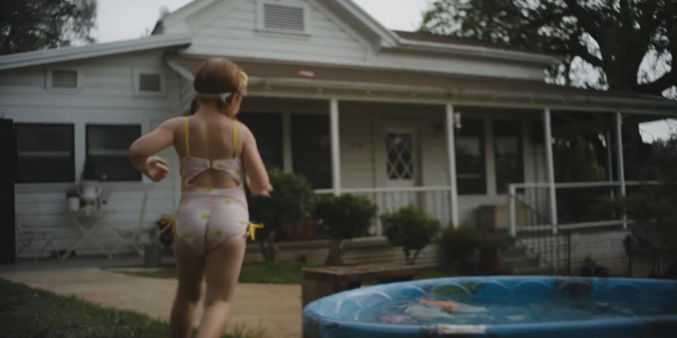 A young girl plays outside by a shallow pool