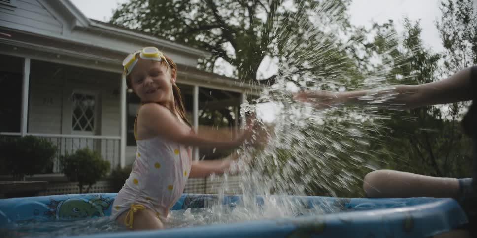 A woman and girl splash in a small pool on the front lawn