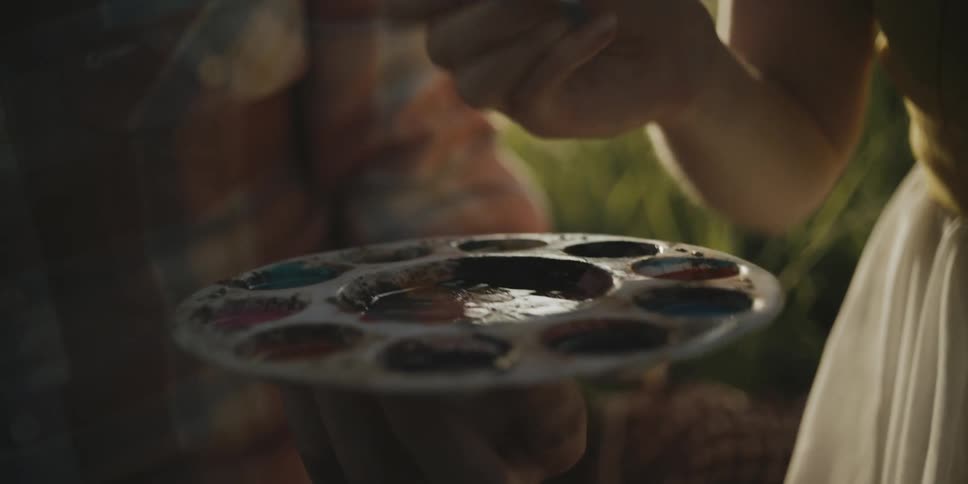 A man is holding a paint pallet as a woman dips a brush into one of the wells