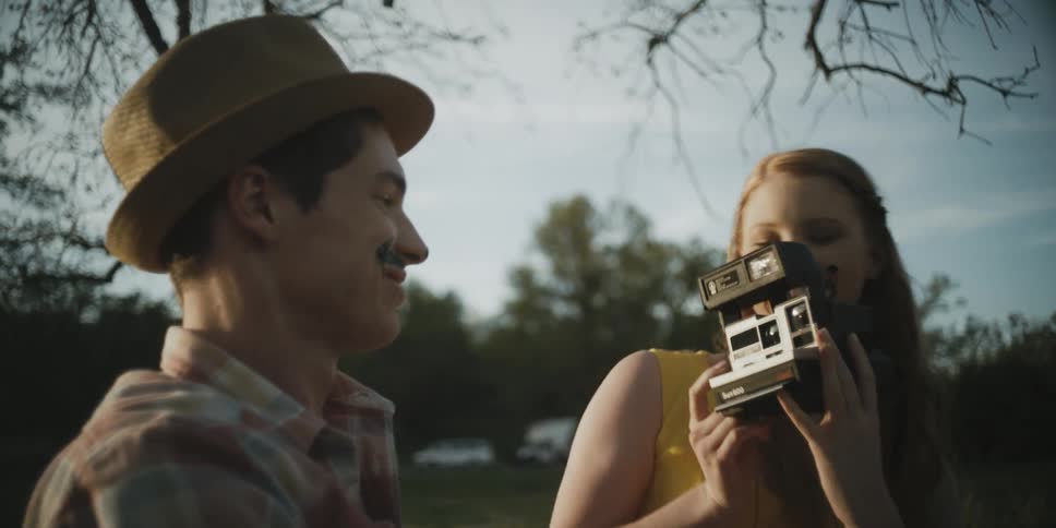 A woman takes a polaroid photo of a man in a hat