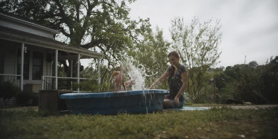 Woman and child splashing in a kiddie pool outside in a yard
